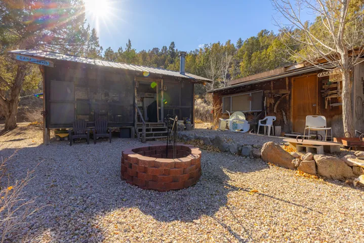 Gravel patio with a brick fire pit, two structures with wood siding, and mature trees on a sloped lot