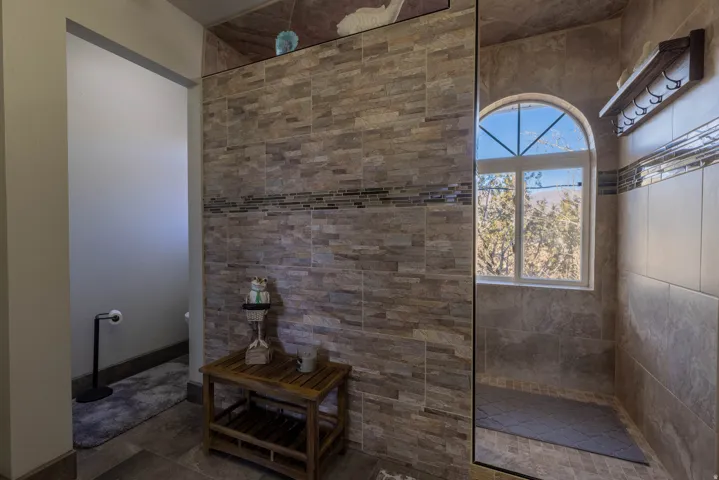 Tiled shower enclosure with a glass panel, arched window, and decorative mosaic tile accent