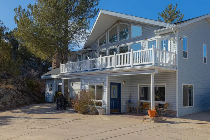 Two-story exterior featuring light blue siding, a prominent second-story balcony with white railing, a ground-level patio, and multiple large windows