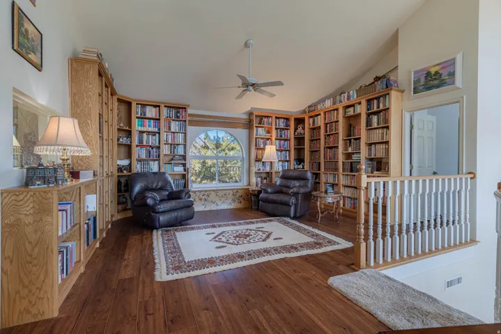Vaulted ceiling over wood-finish flooring, featuring extensive built-in wooden shelving, an arched window, and a ceiling fan