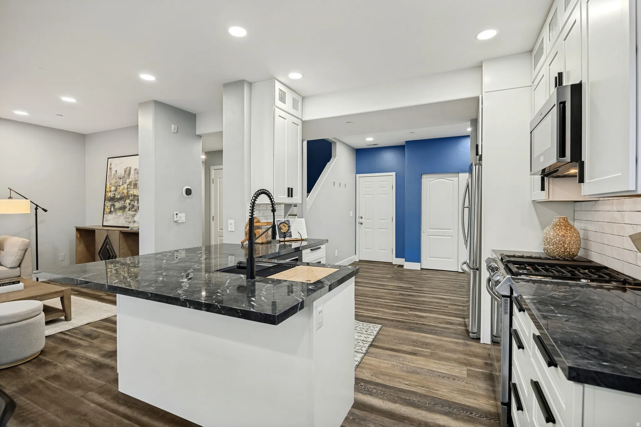 Kitchen featuring dark stone countertops, stainless steel appliances, white cabinetry, and wood-finish flooring