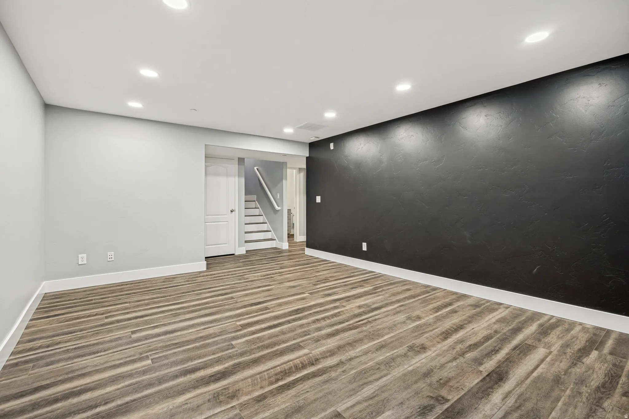 Recessed lighting, wood-finish flooring, white trim, textured accent wall, and painted interior walls