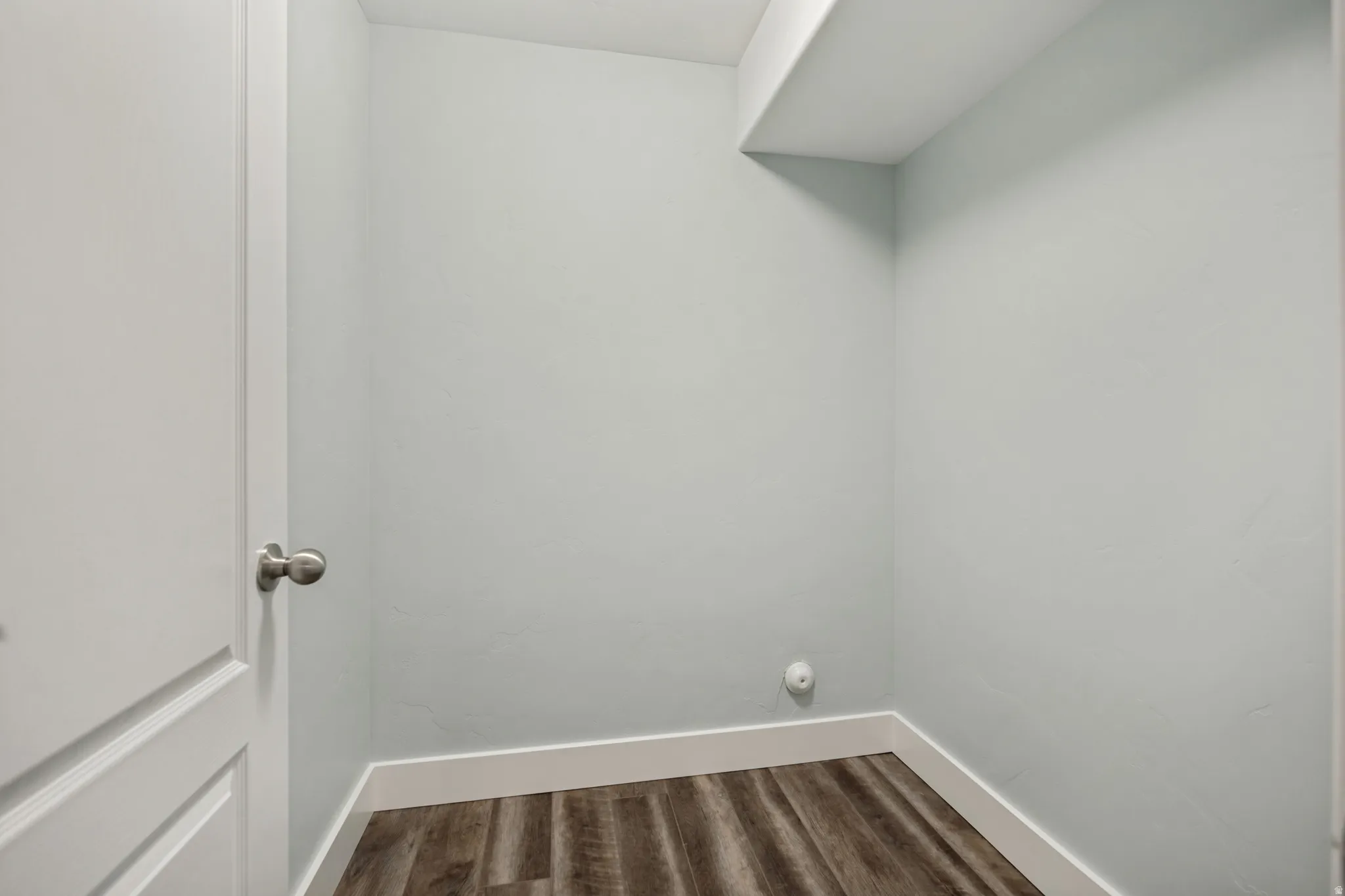Wood-finish flooring with white trim, light-toned walls, and a built-in overhead shelf