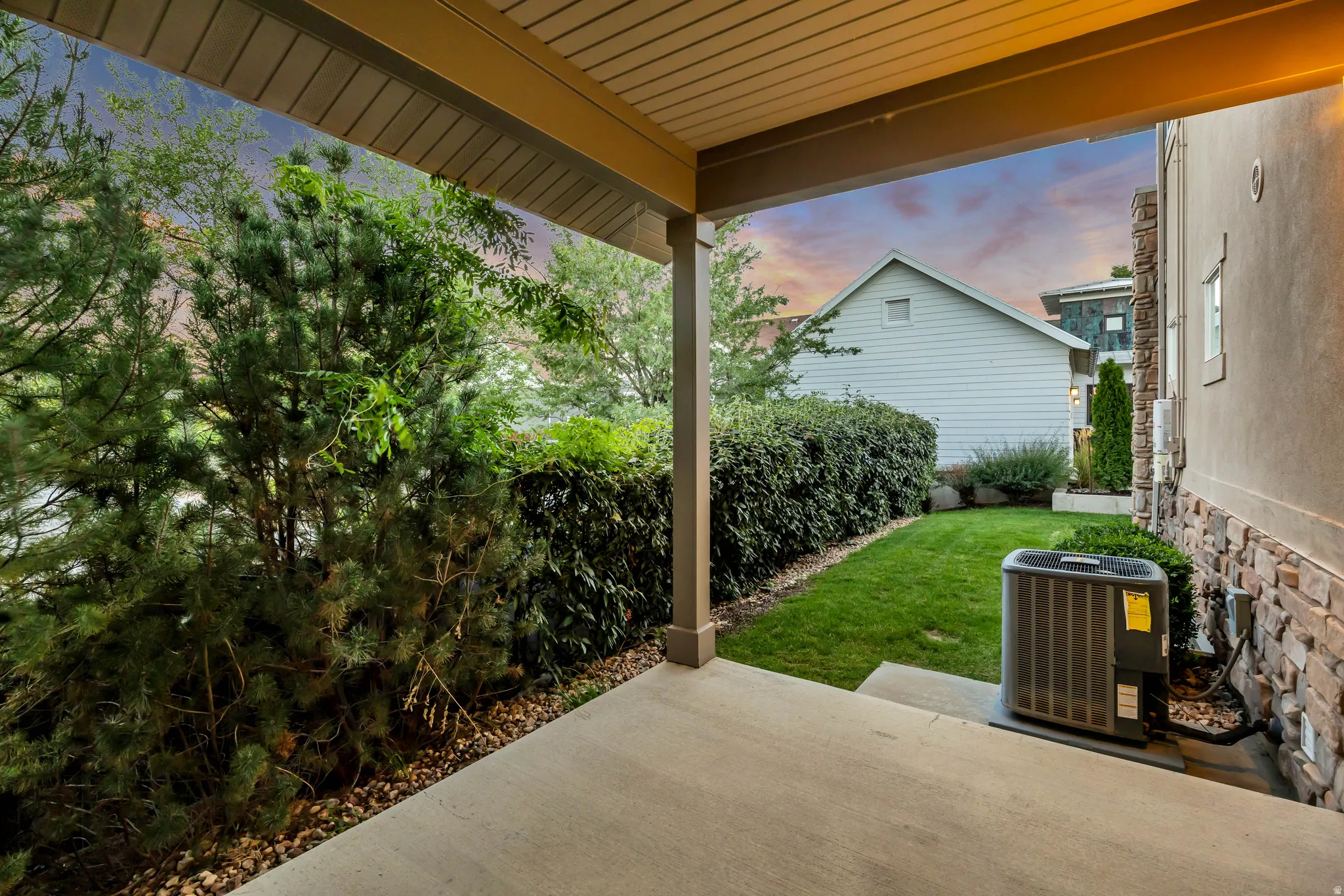 Covered patio with concrete flooring, accented by a manicured lawn and mature landscaping