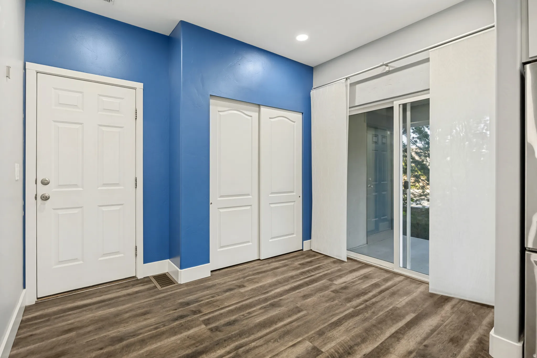 Wood-finish flooring, sliding glass door with privacy panels, white paneled doors, and recessed ceiling lighting