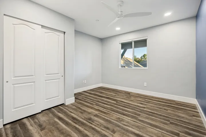 Wood-finish flooring, white sliding closet doors, ceiling fan, recessed lighting, and a sliding window