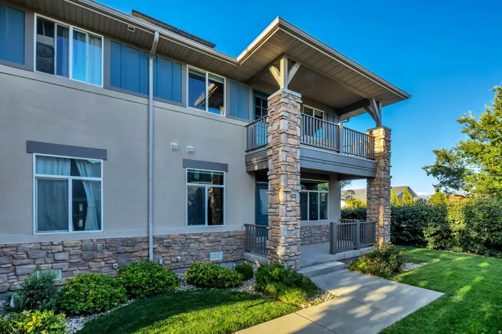 Exterior featuring a stone facade, stucco siding, a covered balcony, a covered porch, and a concrete walkway