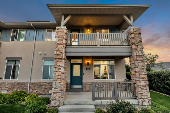 Stucco exterior with stacked stone accents, a covered front porch, and an upper-level balcony with wood railings
