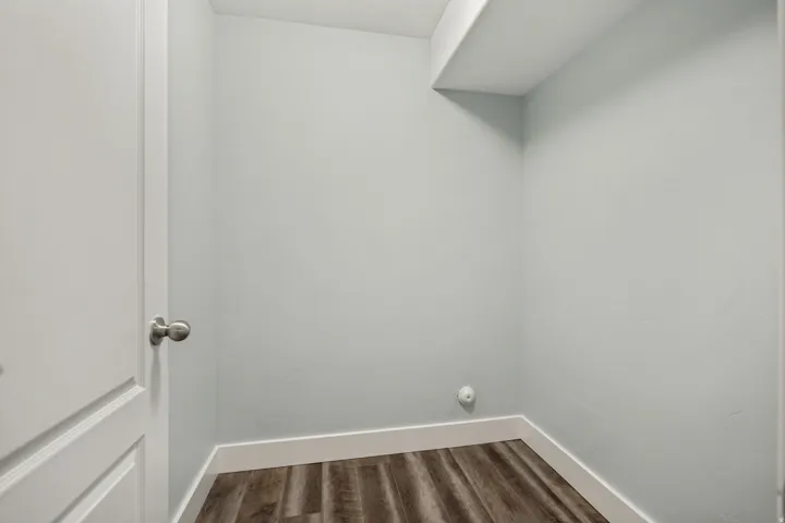 Wood-finish flooring with white trim, light-toned walls, and a built-in overhead shelf