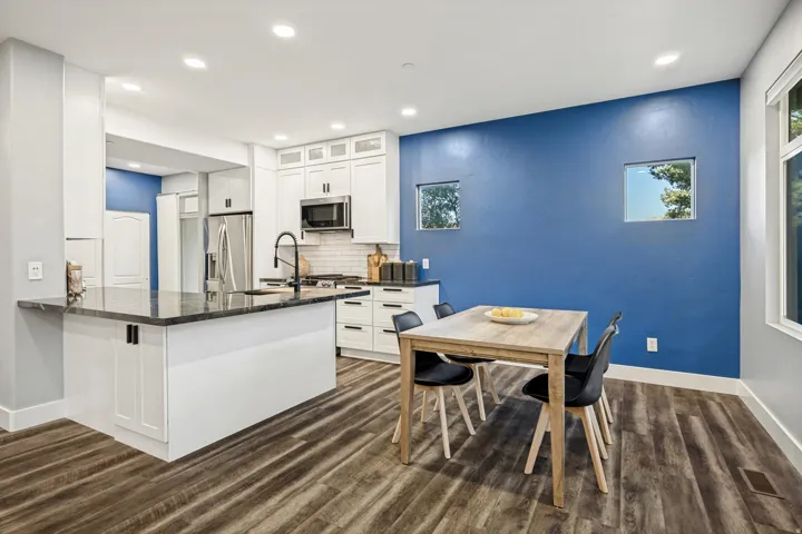 Spacious kitchen and dining area featuring white cabinetry, a large kitchen island with a dark countertop, wood-finish flooring, and recessed lighting