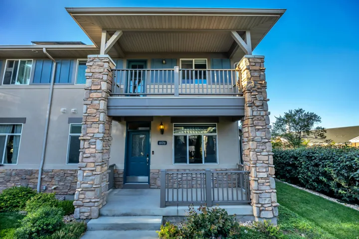 Stacked stone facade with an upper-level balcony, a lower-level patio, and a teal entry door