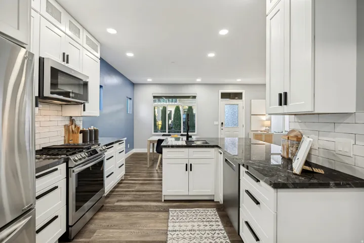 Modern kitchen featuring white cabinetry, black countertops, stainless steel appliances, and wood-finish flooring
