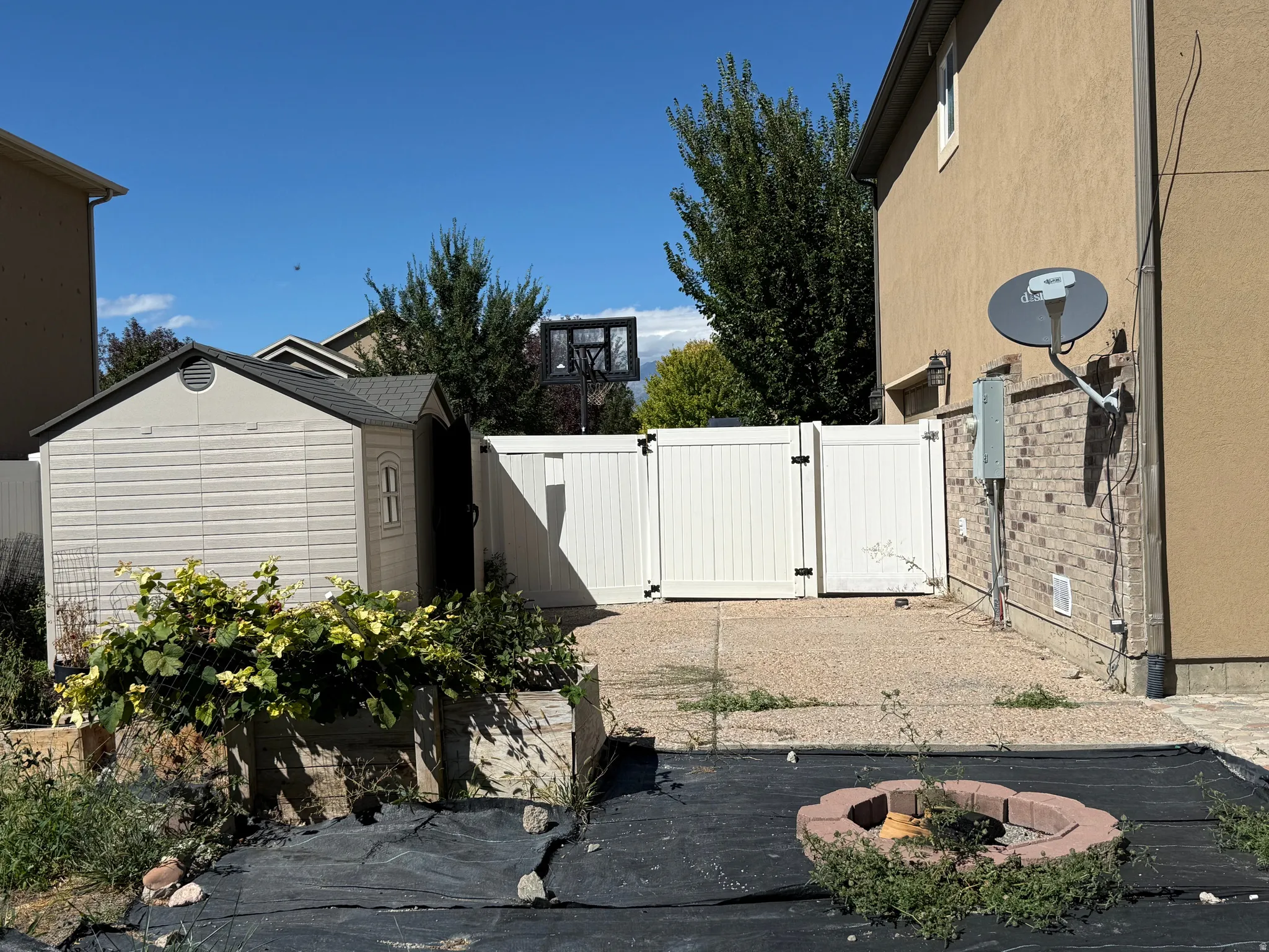 Backyard space featuring a plastic shed, white vinyl fencing, brick veneer detailing, and a stone-ringed fire pit