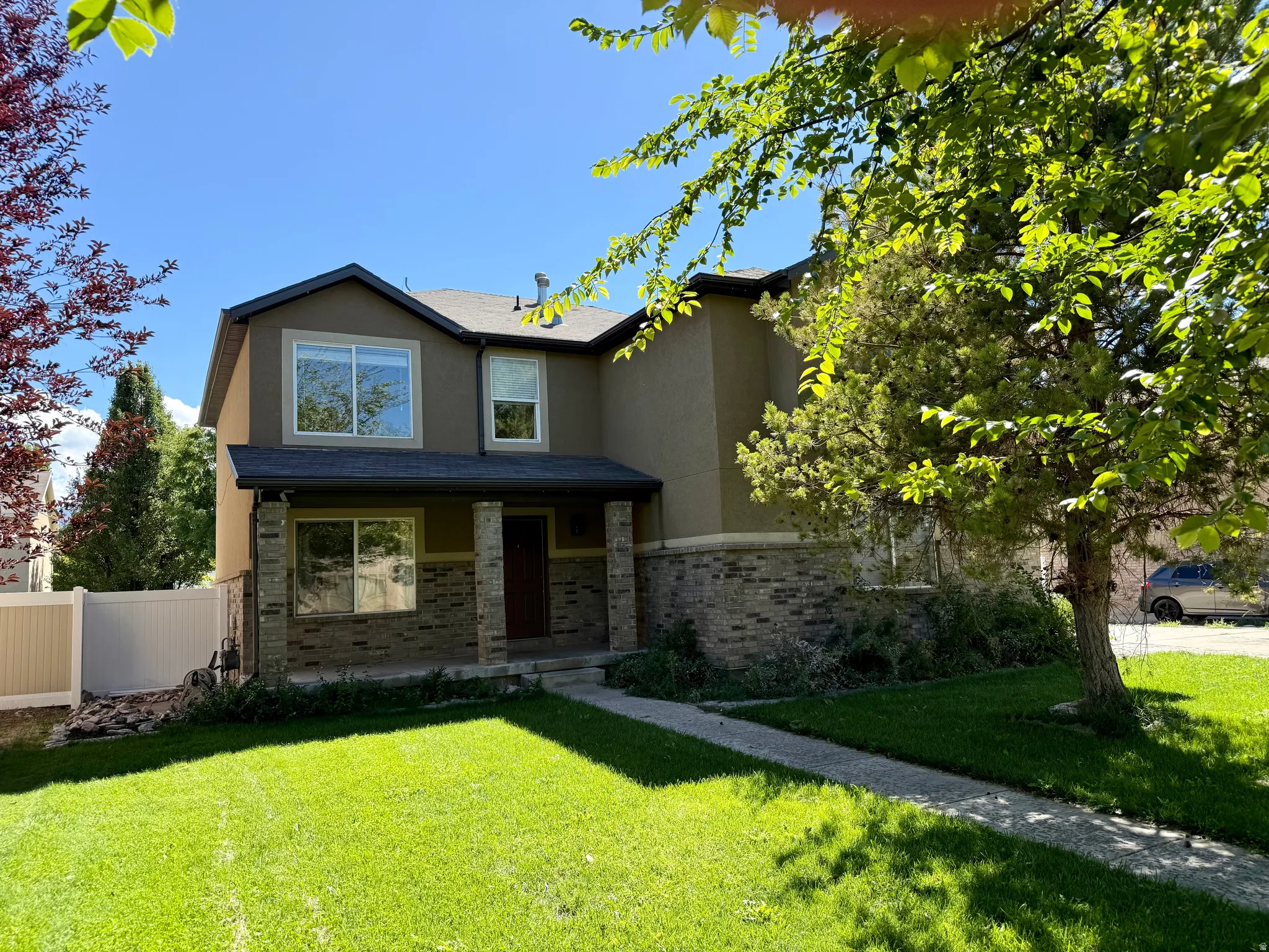 Two-story residence featuring a stucco and stone exterior, a covered entry porch with columns, a dark roof, and a front lawn with a concrete pathway