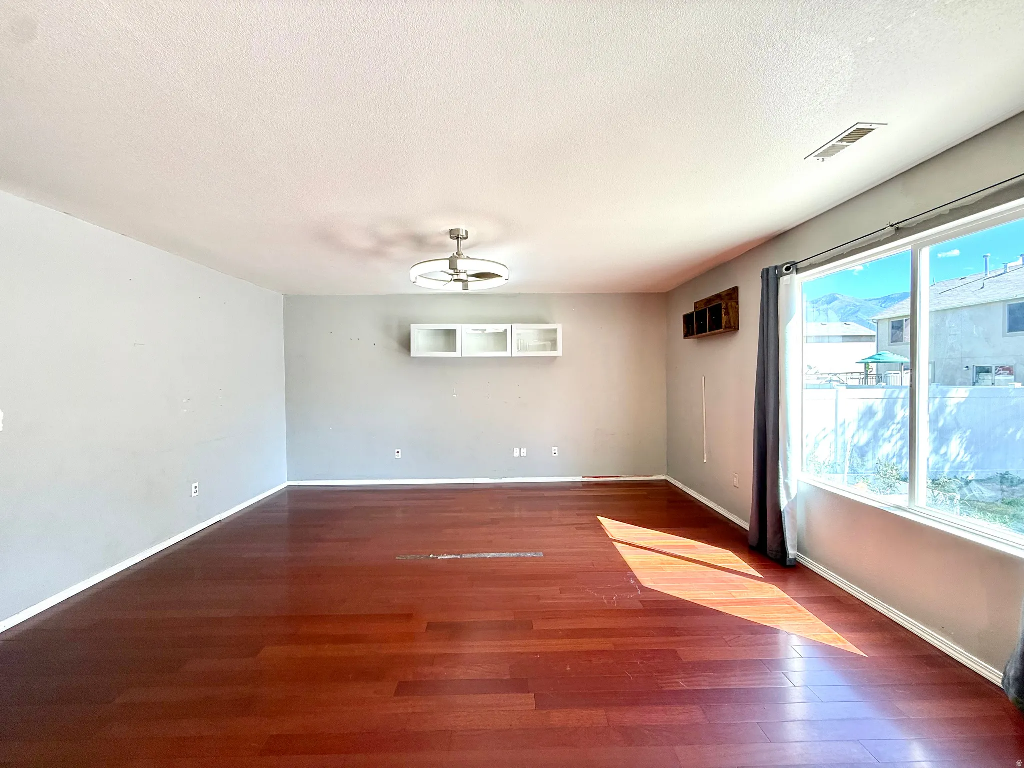 Wood-finish flooring, ceiling fan with integrated lighting, wall-mounted shelving, and large windows