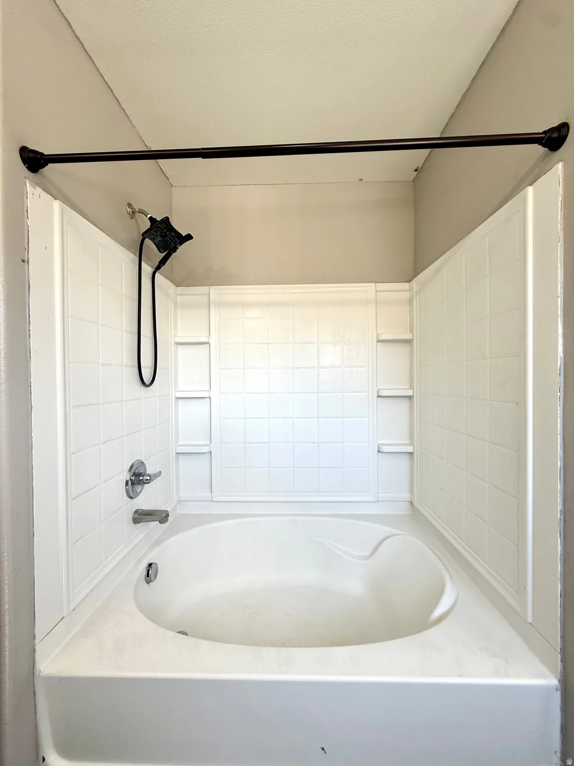 Built-in bathtub with white tile surround, chrome fixtures, and integrated shelving