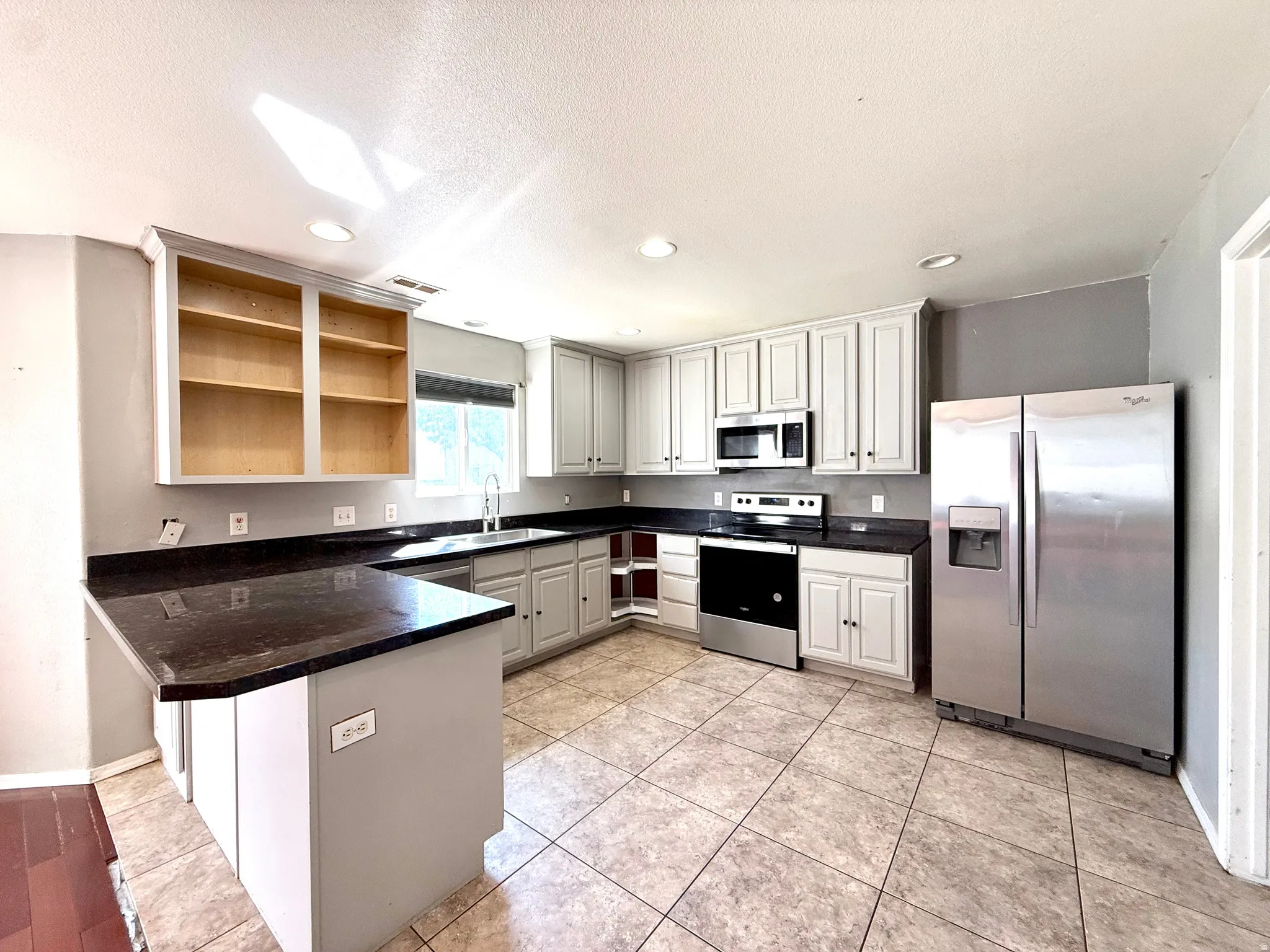 Kitchen featuring dark countertops, stainless steel appliances, light-toned cabinetry, a built-in microwave, and tile flooring