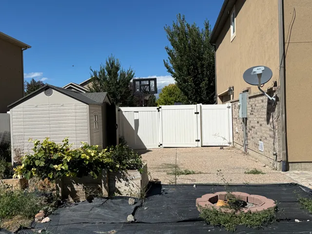 Backyard space featuring a plastic shed, white vinyl fencing, brick veneer detailing, and a stone-ringed fire pit