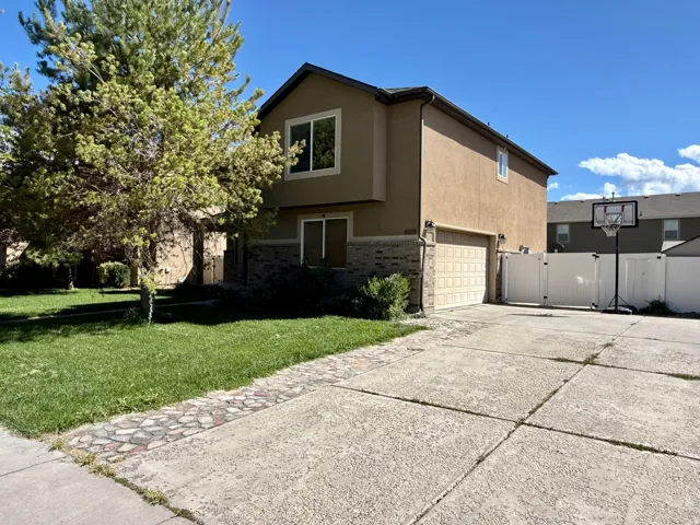 Two-story stucco exterior with stone veneer accents, an attached garage, a privacy fence, and a concrete driveway