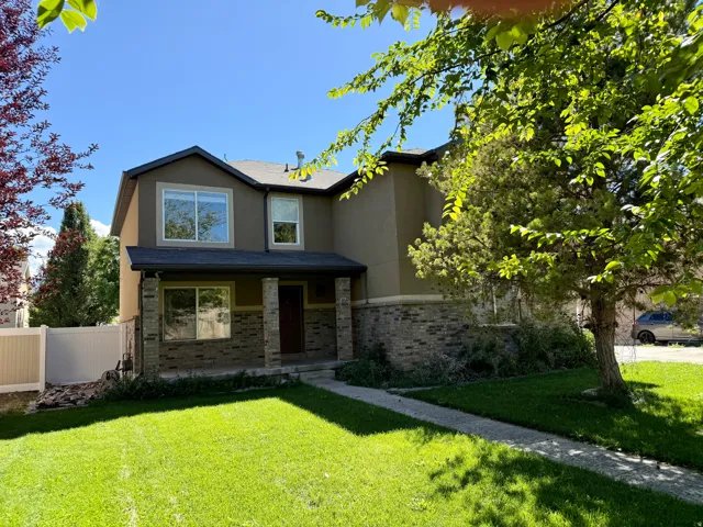 Two-story residence featuring a stucco and stone exterior, a covered entry porch with columns, a dark roof, and a front lawn with a concrete pathway