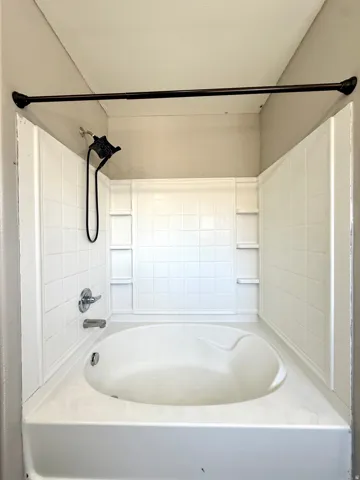 Built-in bathtub with white tile surround, chrome fixtures, and integrated shelving