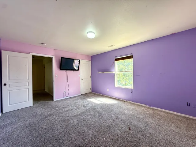 Wall-mounted television bracket, window with blinds, overhead flush-mount light fixture, and textured carpeting