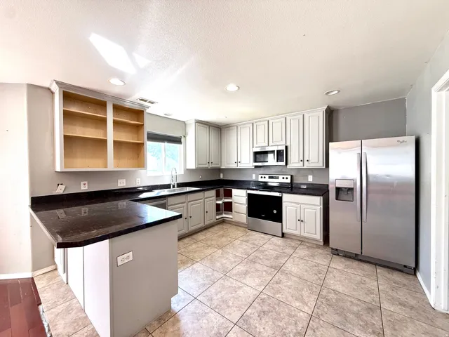 Kitchen featuring dark countertops, stainless steel appliances, light-toned cabinetry, a built-in microwave, and tile flooring