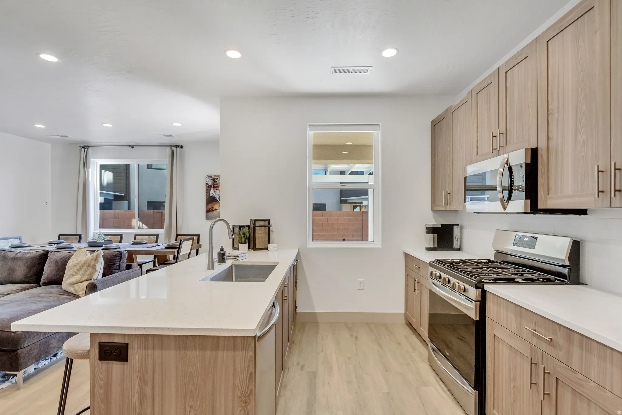 Kitchen featuring wood-finish cabinetry, stainless steel appliances, a large island with a sink, and light-toned countertops