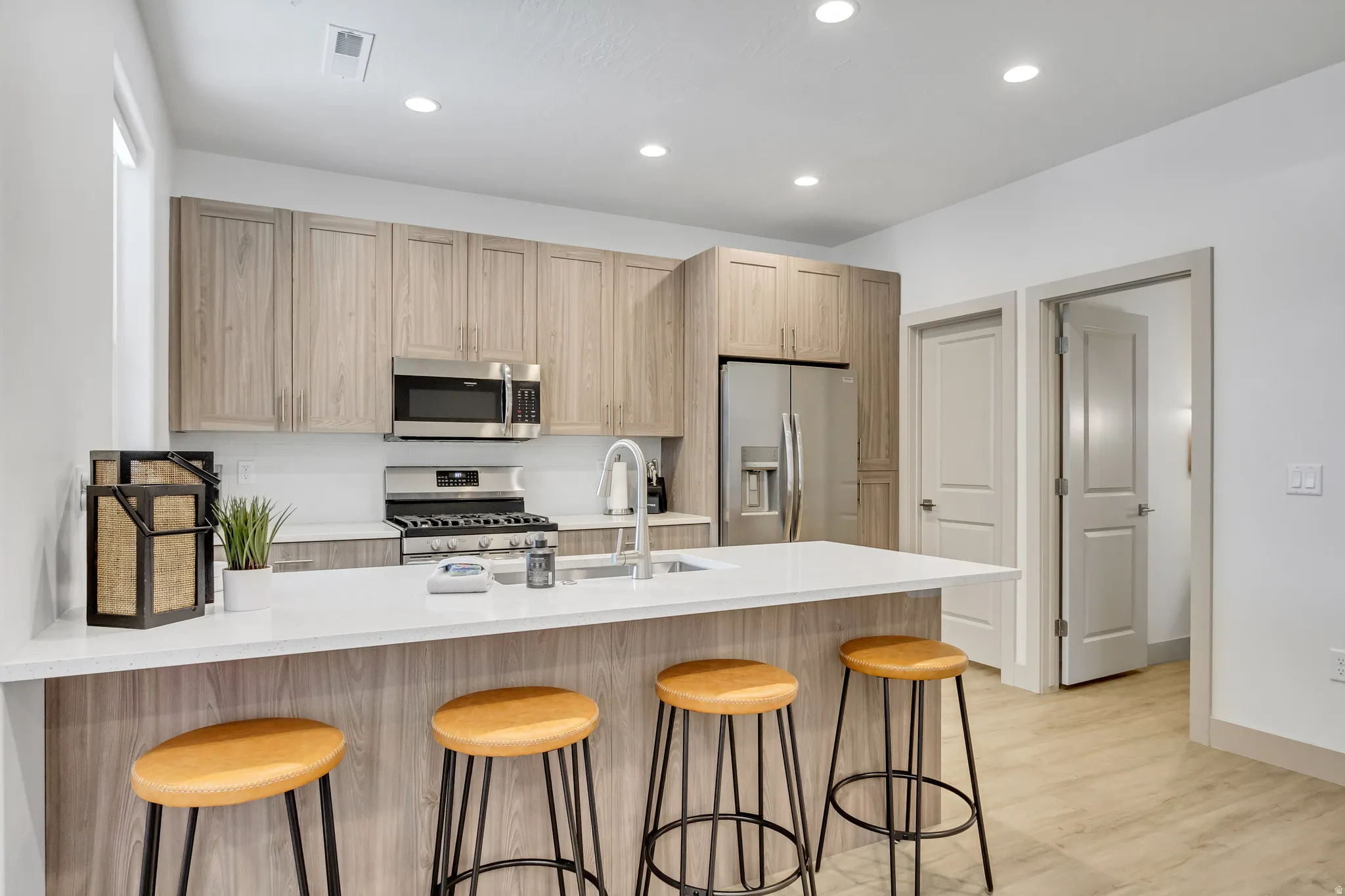 Kitchen featuring wood-finish cabinetry, stainless steel appliances, a white countertop island with seating, and recessed lighting
