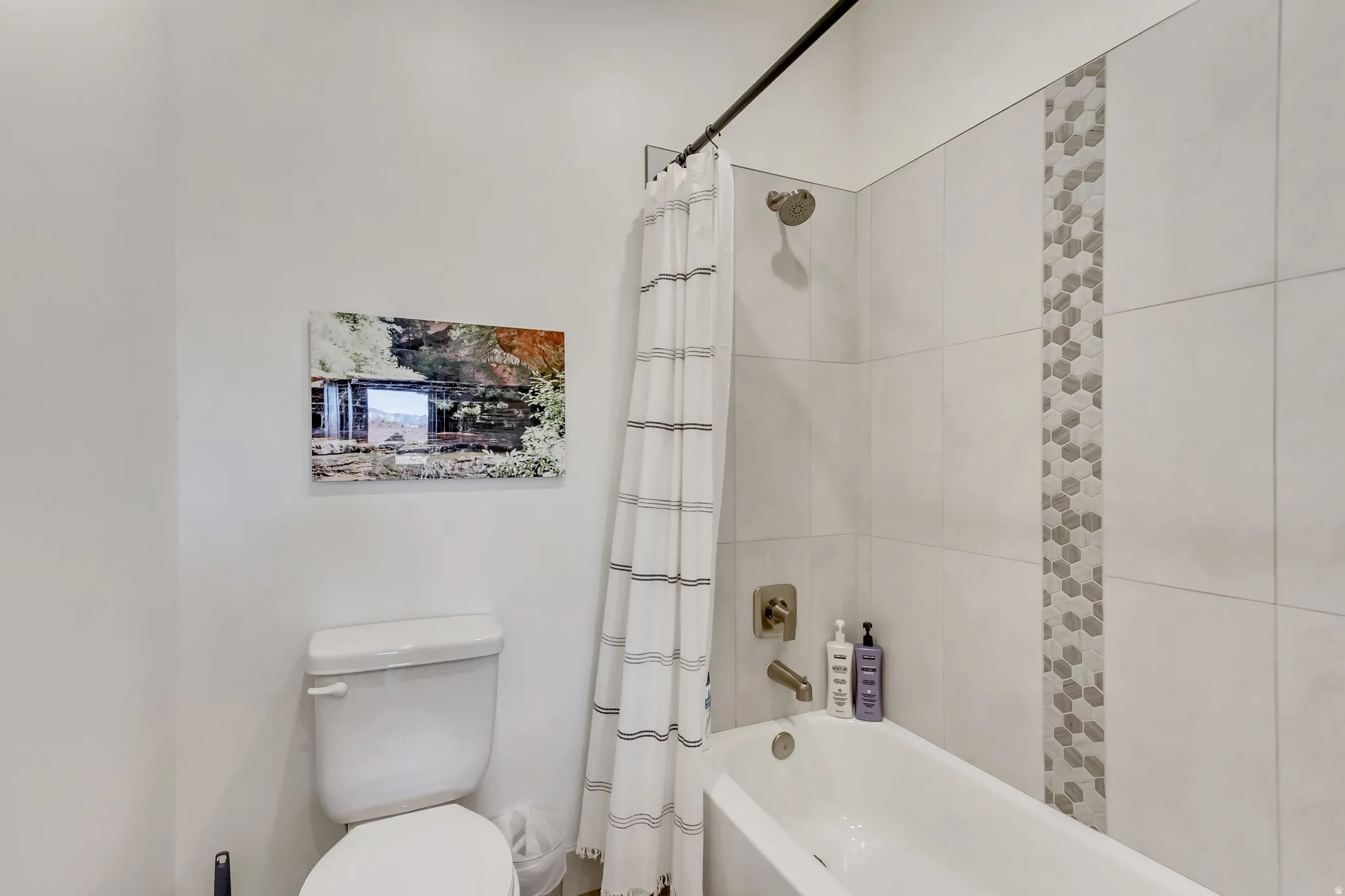 Bathtub and shower with light-toned tiled surround, accent mosaic tile strip, and brushed nickel fixtures