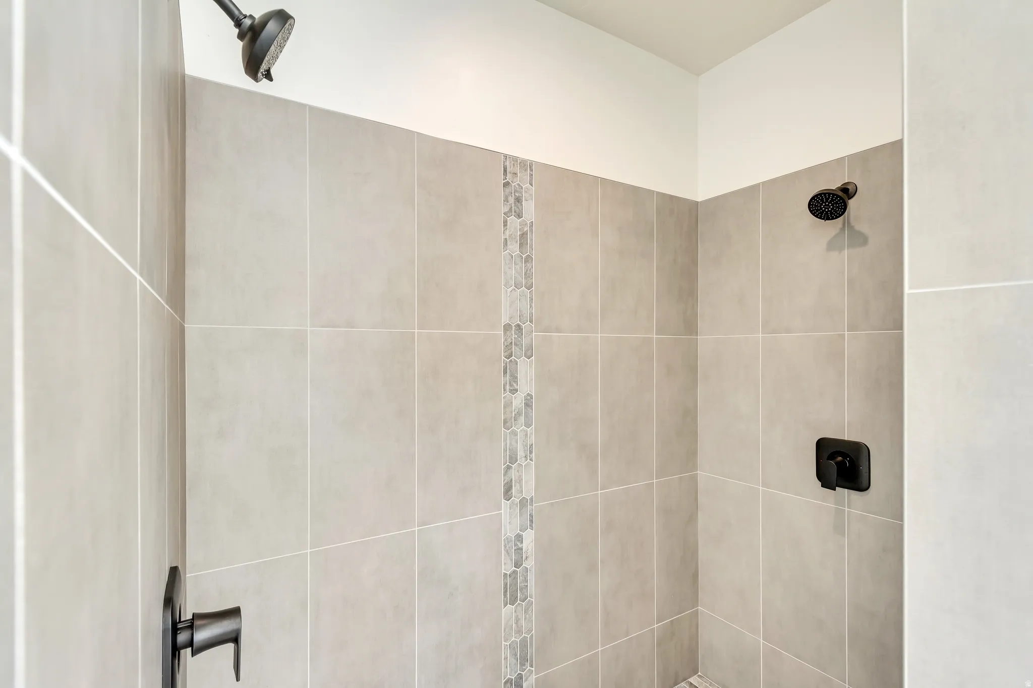Matte black shower fixtures with a rainfall showerhead, large format tile walls, and a decorative tile accent strip