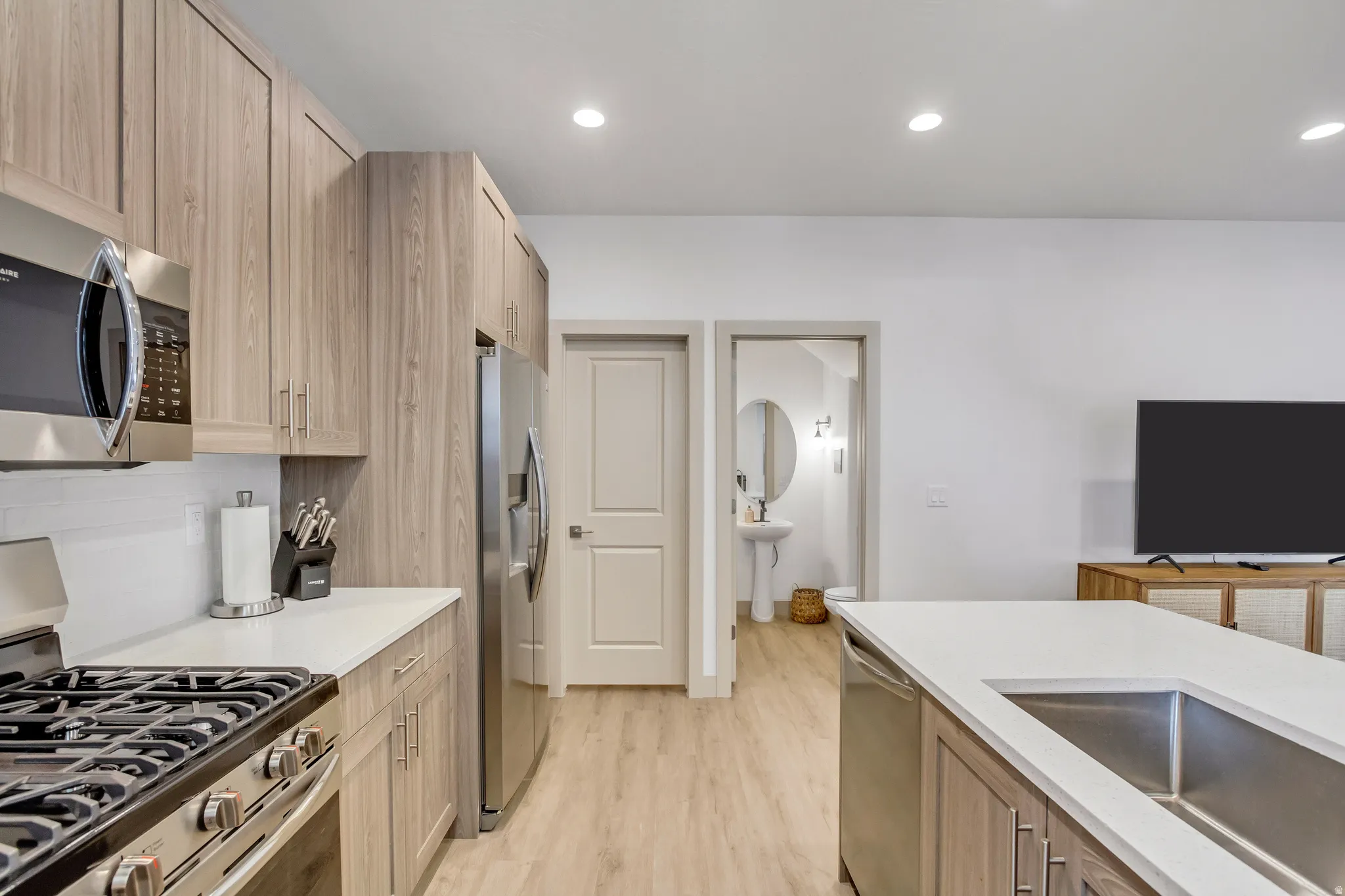 Contemporary kitchen featuring wood-finish cabinetry, stainless steel appliances, a gas range, and a kitchen island with an undermount sink and solid surface countertops