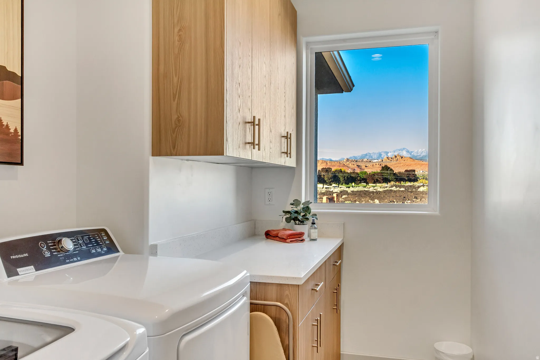Light wood-finish cabinetry, white countertop, and a window with a natural landscape