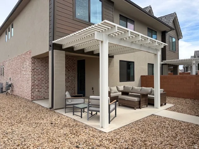 Rear patio with a white pergola, concrete surface, and surrounding rock landscaping