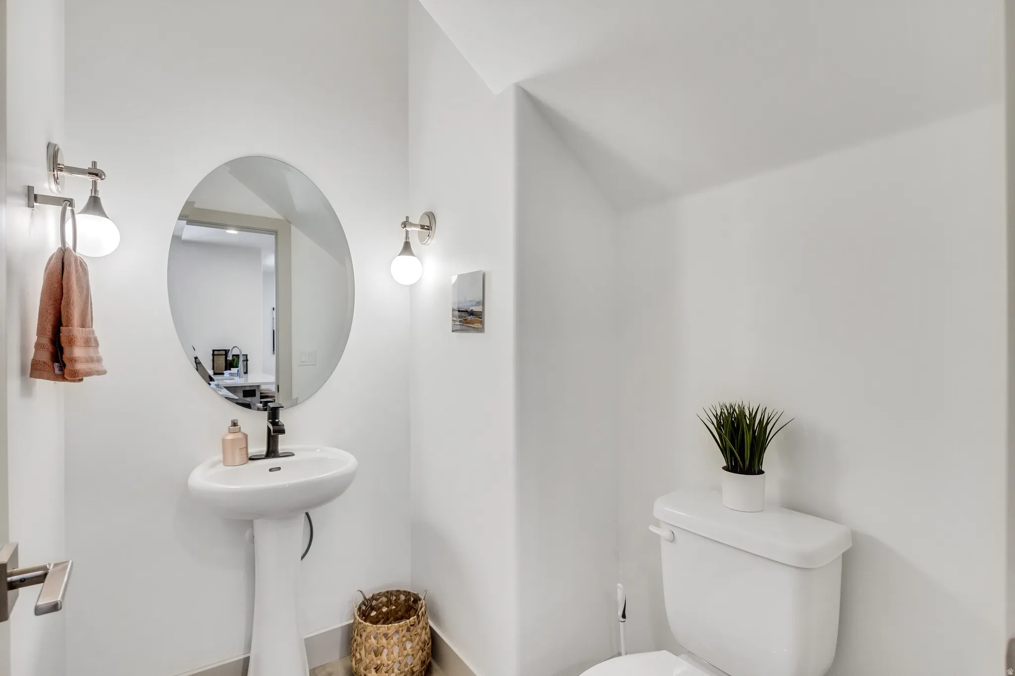 Pedestal sink with a matte black faucet, oval mirror, and wall-mounted light fixtures