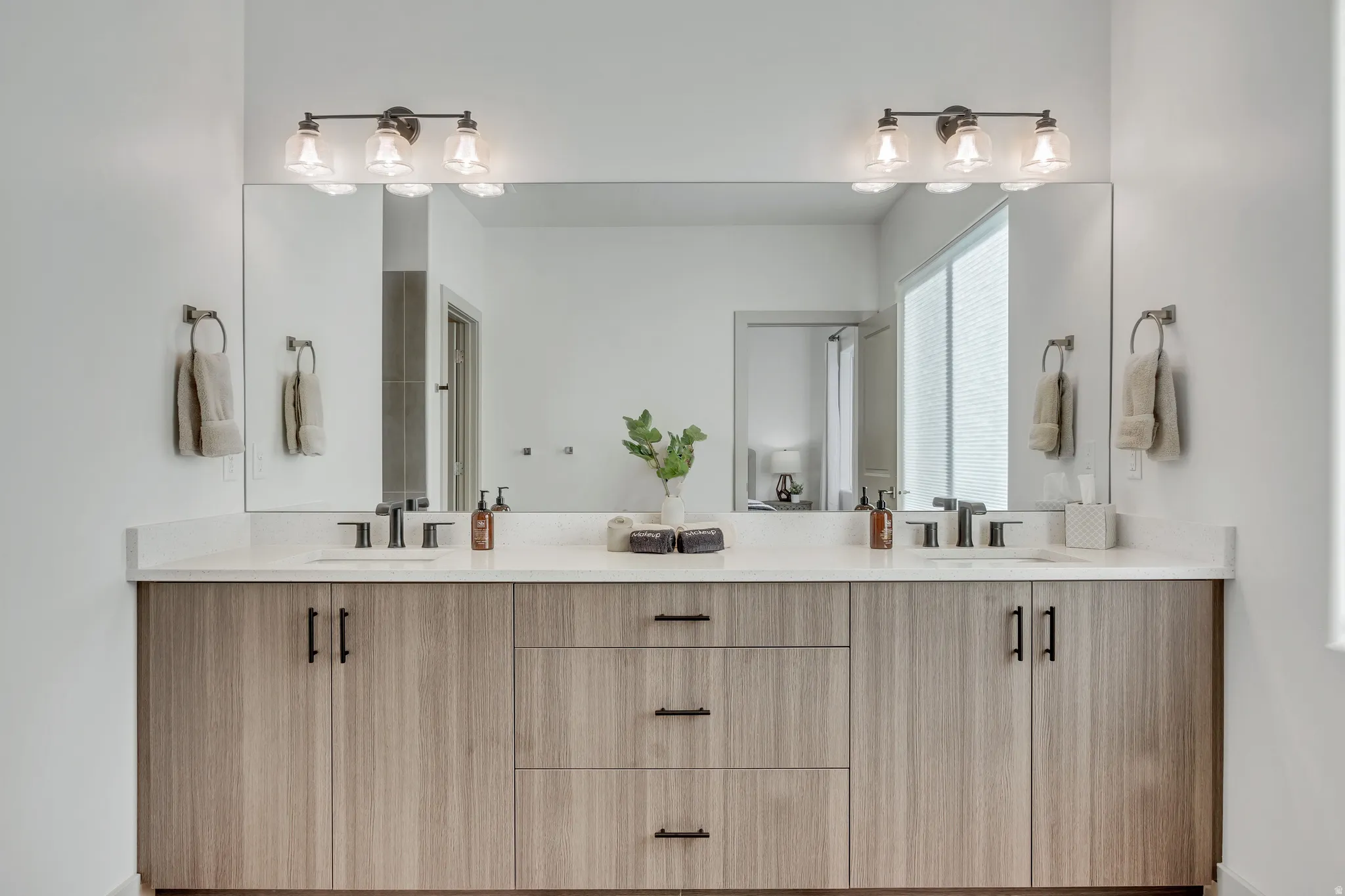 Dual-sink bathroom vanity featuring wood-finish cabinetry with black hardware, white quartz countertops, and matte black faucets