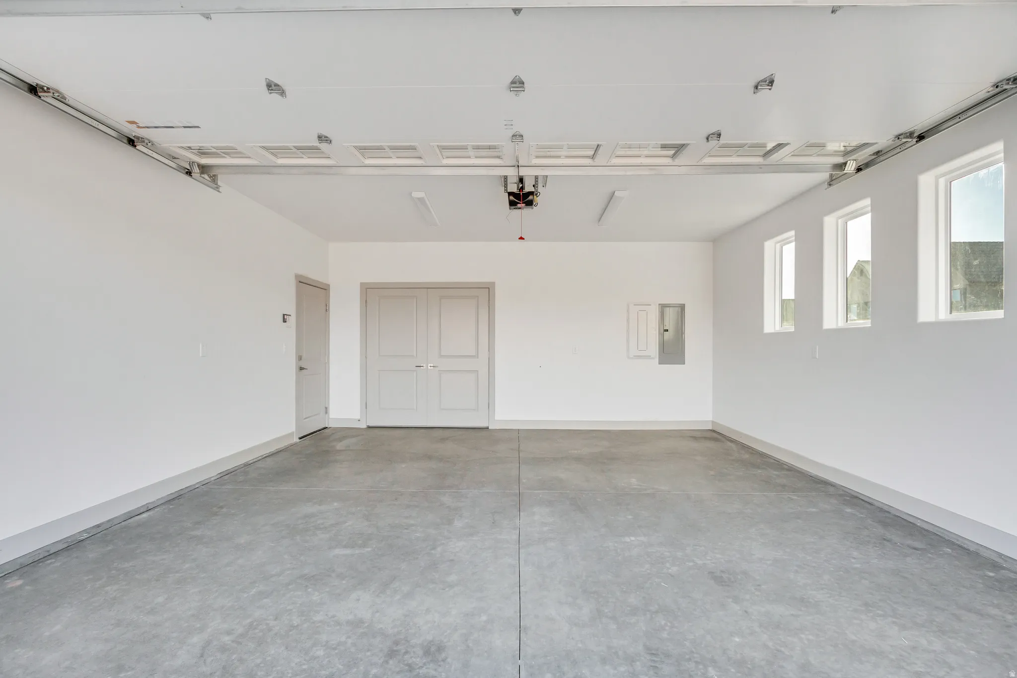 Concrete flooring, white walls, three rectangular windows, an interior door, and double doors