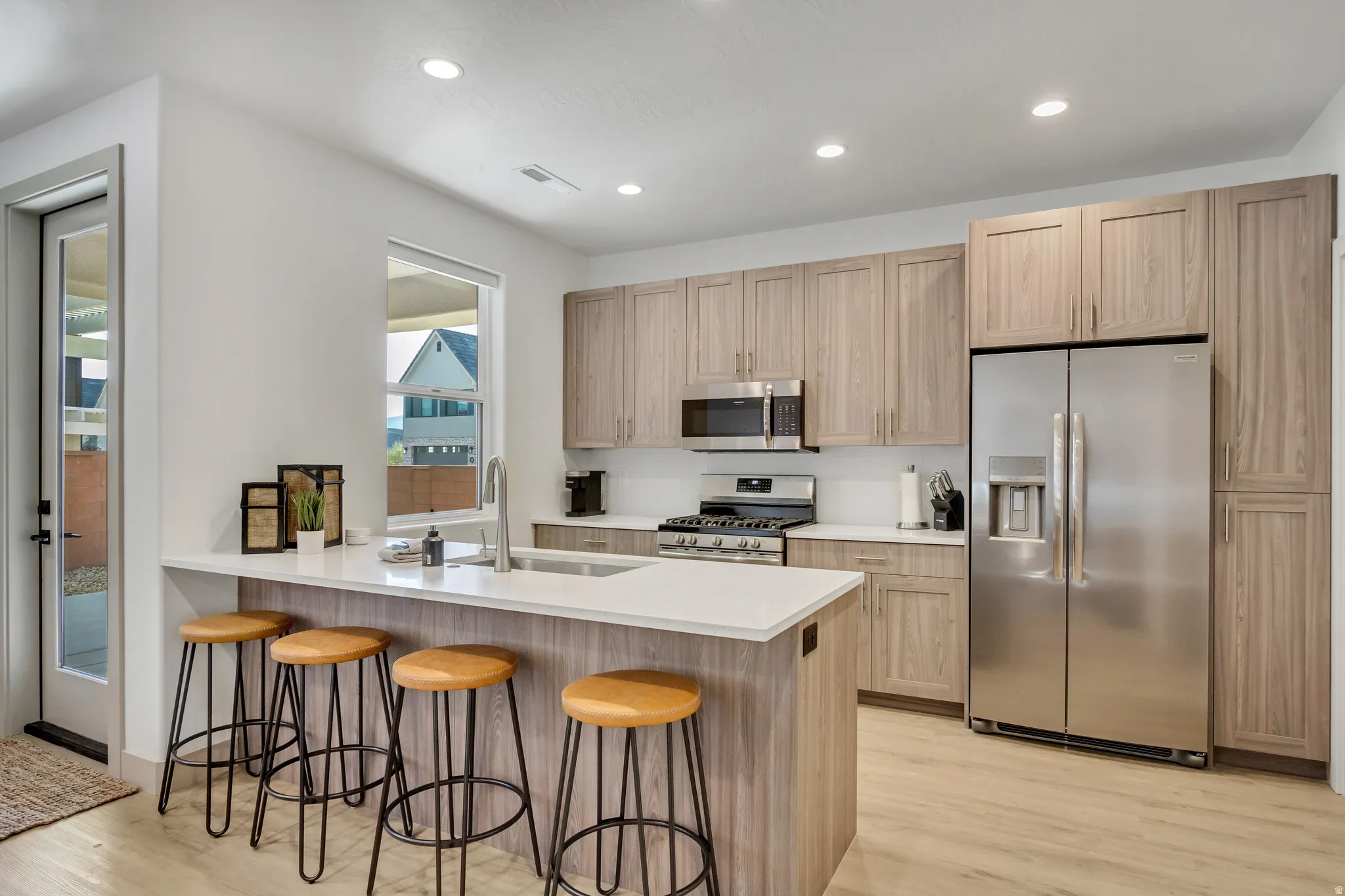 Kitchen featuring wood-finish cabinetry, stainless steel appliances, a center island with counter seating, recessed lighting, and a full-light exterior door