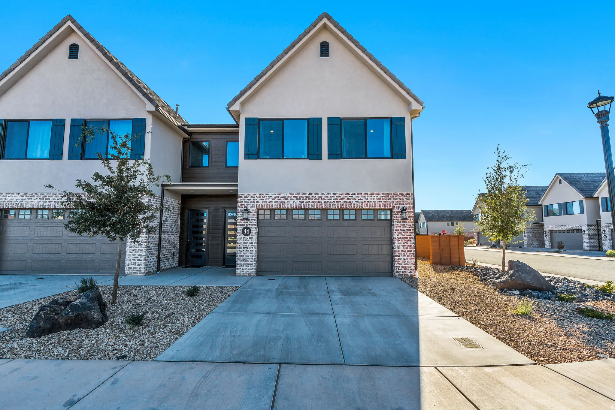 Modern stucco exterior with brick accents, attached two-car garage, contemporary front door, shuttered windows, and a landscaped rock garden