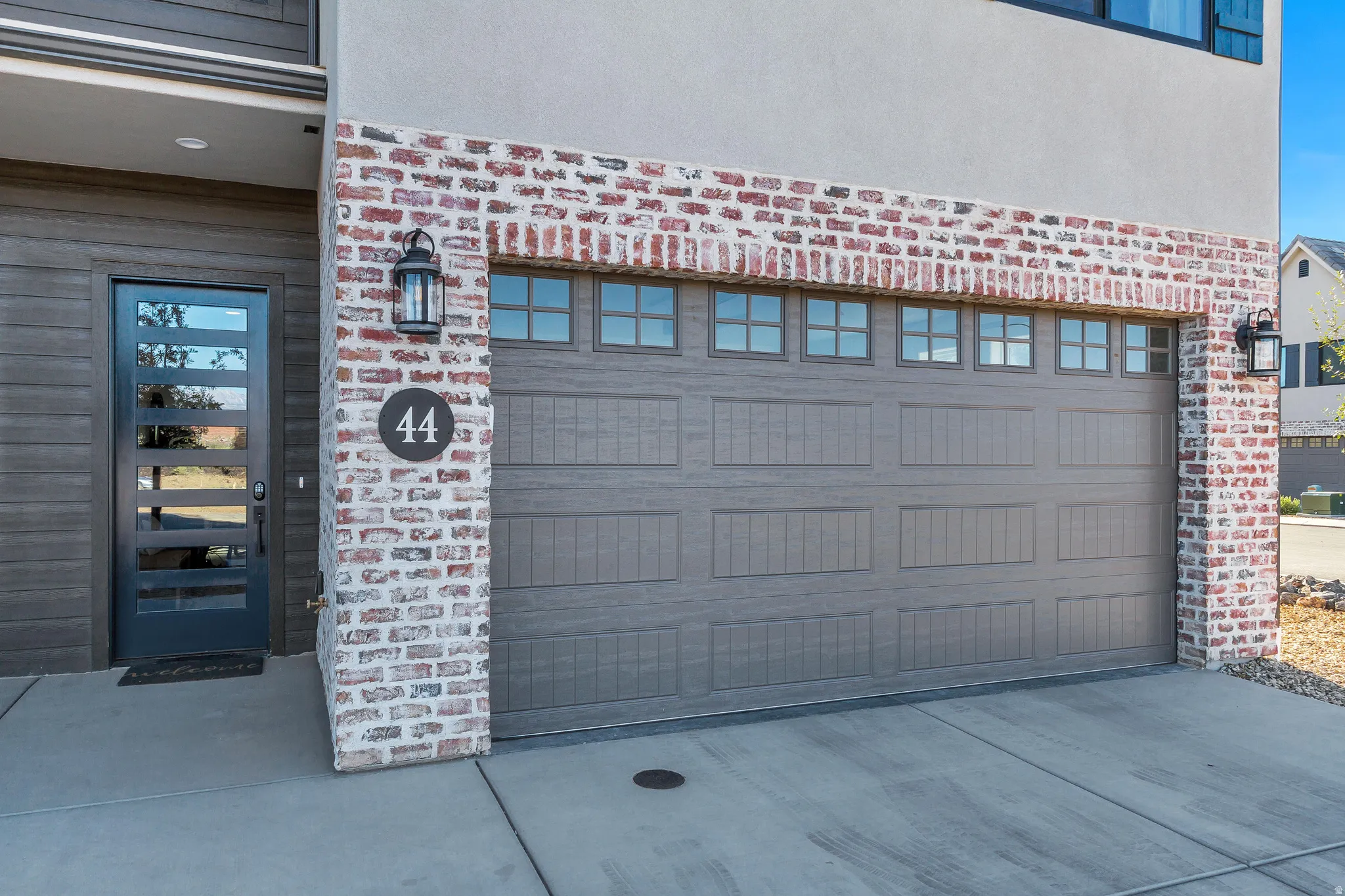 Contemporary exterior featuring a panel-front garage door with transom windows, a modern glass-paneled entry door, and mixed material siding with brick accents