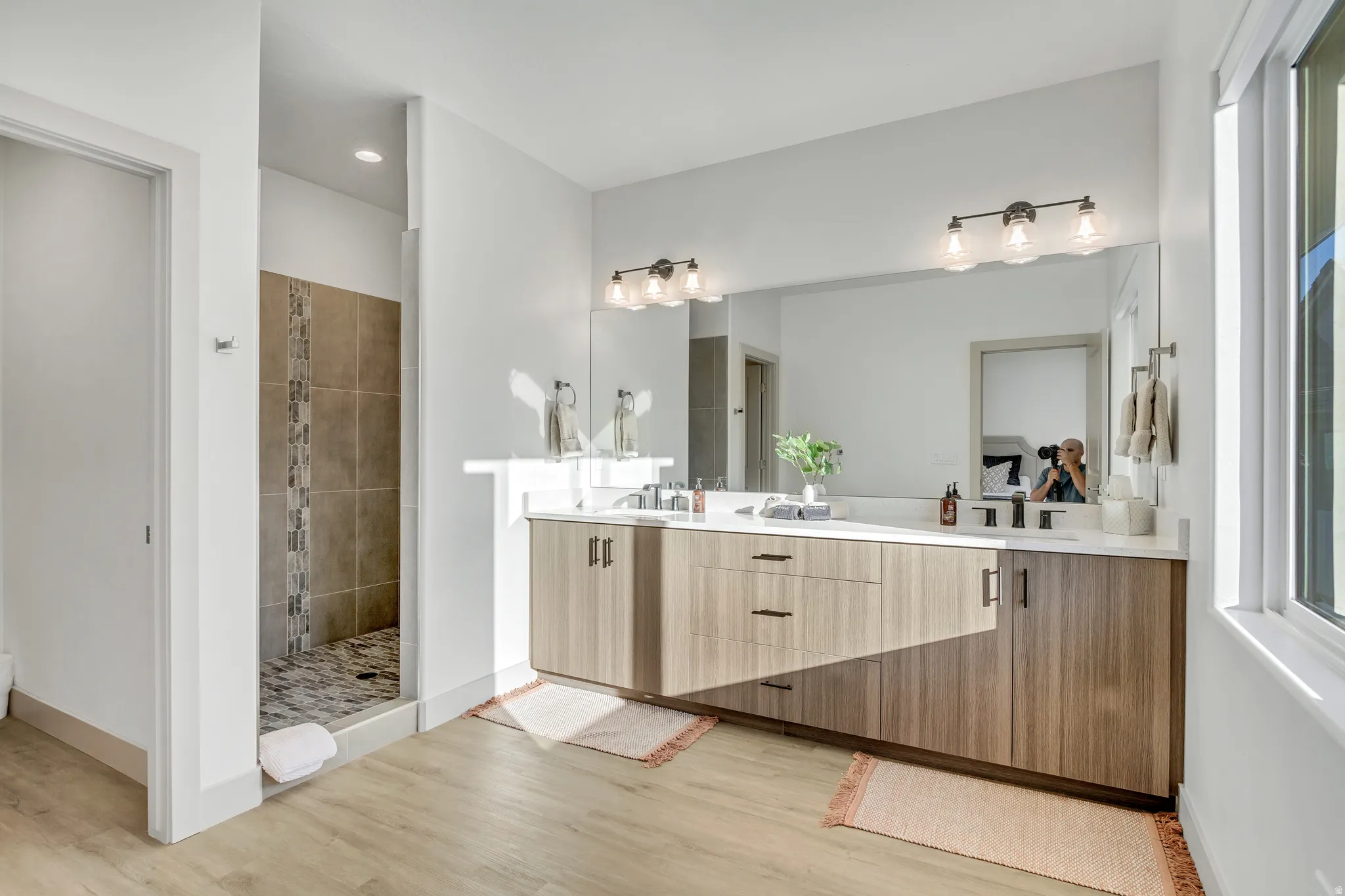 Spacious bathroom featuring a dual vanity with wood-finish cabinetry, a large mirror, and a walk-in shower with tiled walls and floor