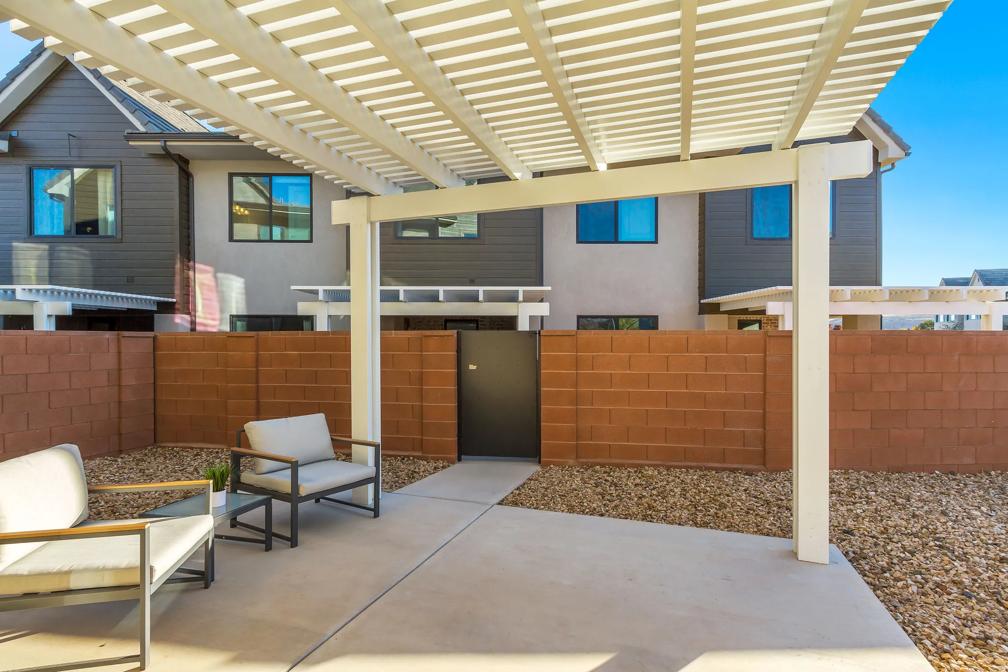 Private patio featuring a slatted pergola, concrete paving, and a block wall with a dark gate