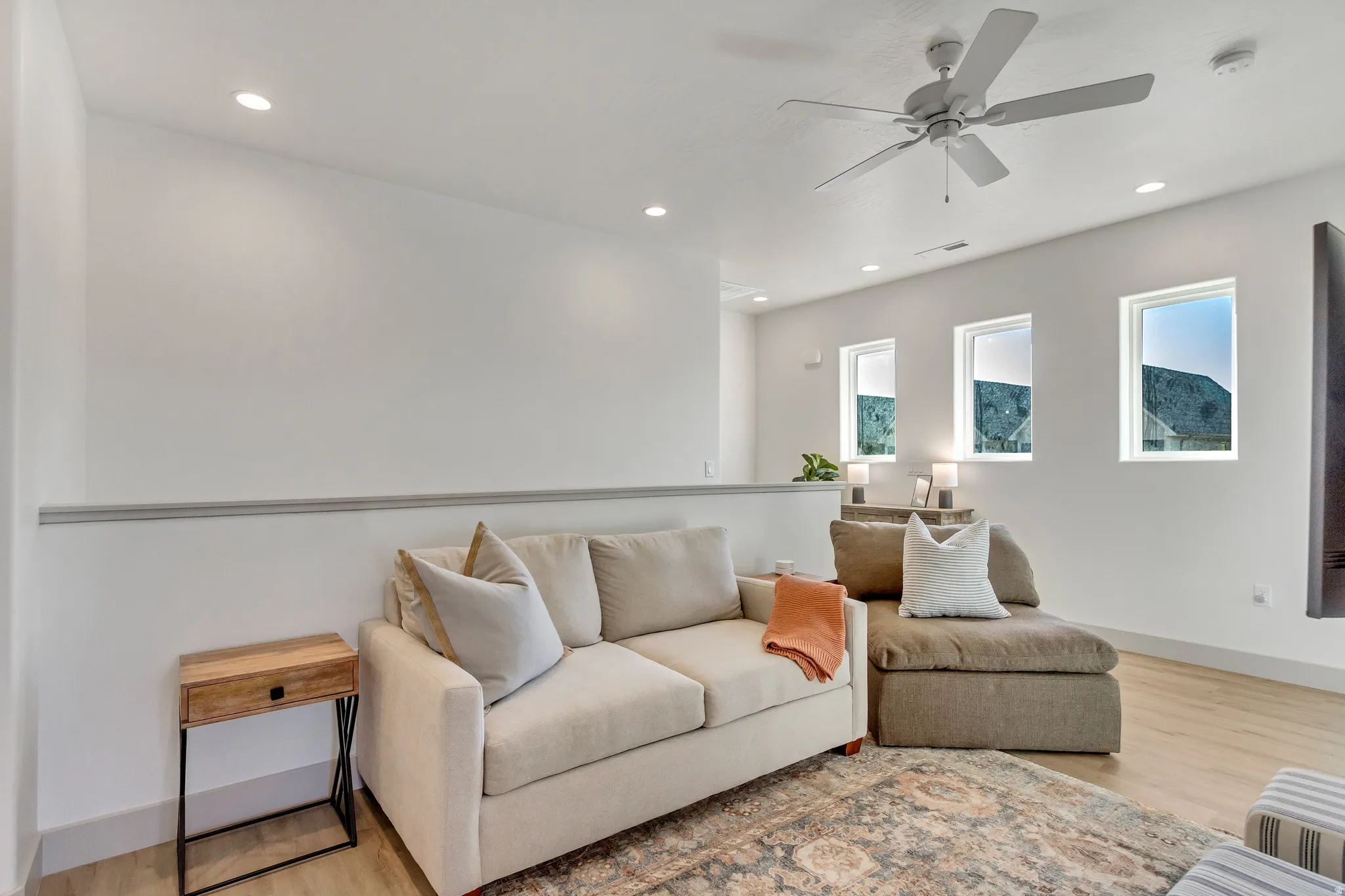 Recessed lighting, ceiling fan, three windows, and light wood-finish flooring