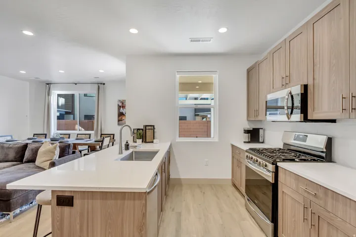 Kitchen featuring wood-finish cabinetry, stainless steel appliances, a large island with a sink, and light-toned countertops