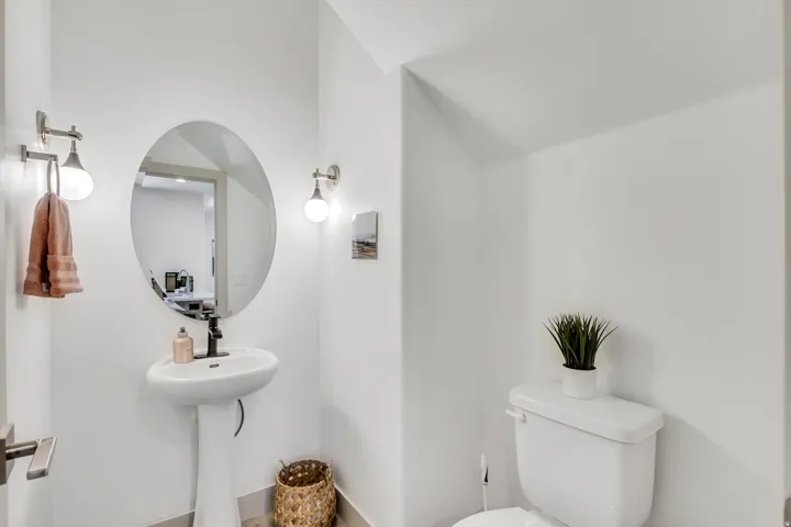 Pedestal sink with a matte black faucet, oval mirror, and wall-mounted light fixtures