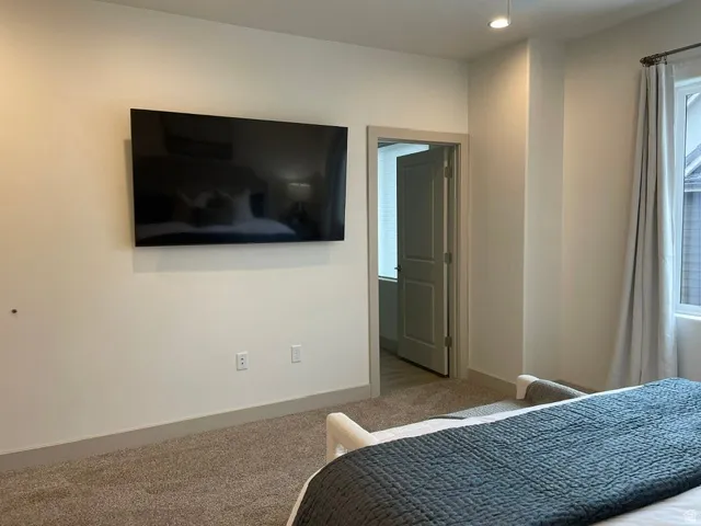 Wall-mounted television, recessed lighting, and a modern window with drapery