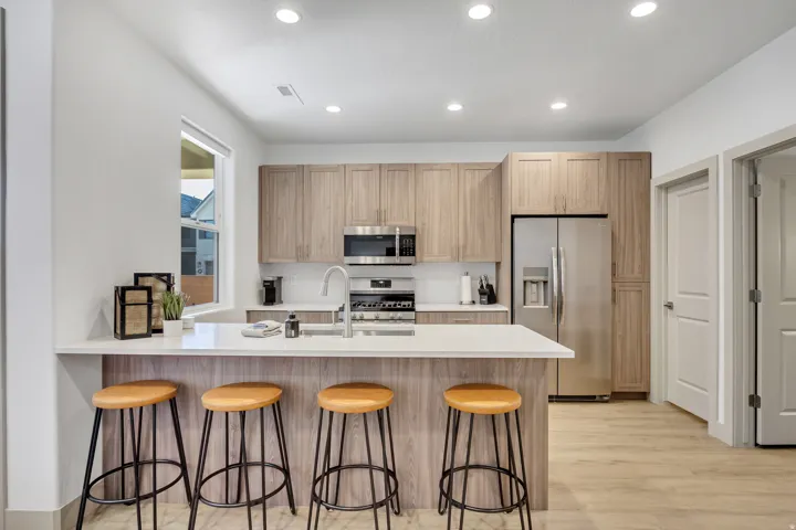 Modern kitchen featuring light wood-finish cabinetry, stainless steel appliances, a white countertop island, and recessed lighting