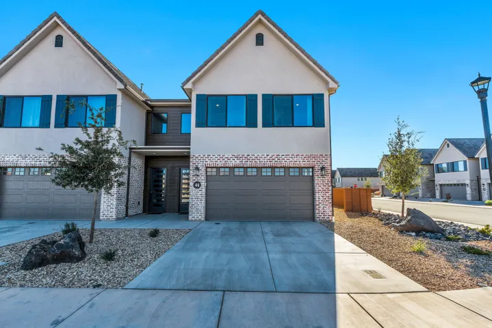 Modern stucco exterior with brick accents, attached two-car garage, contemporary front door, shuttered windows, and a landscaped rock garden