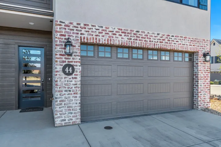 Contemporary exterior featuring a panel-front garage door with transom windows, a modern glass-paneled entry door, and mixed material siding with brick accents
