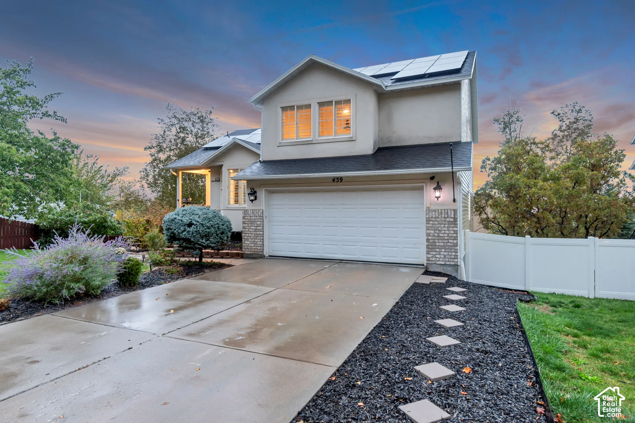 Two-story residence featuring a concrete driveway, attached garage, rooftop solar panels, stone masonry accents, and a white privacy fence